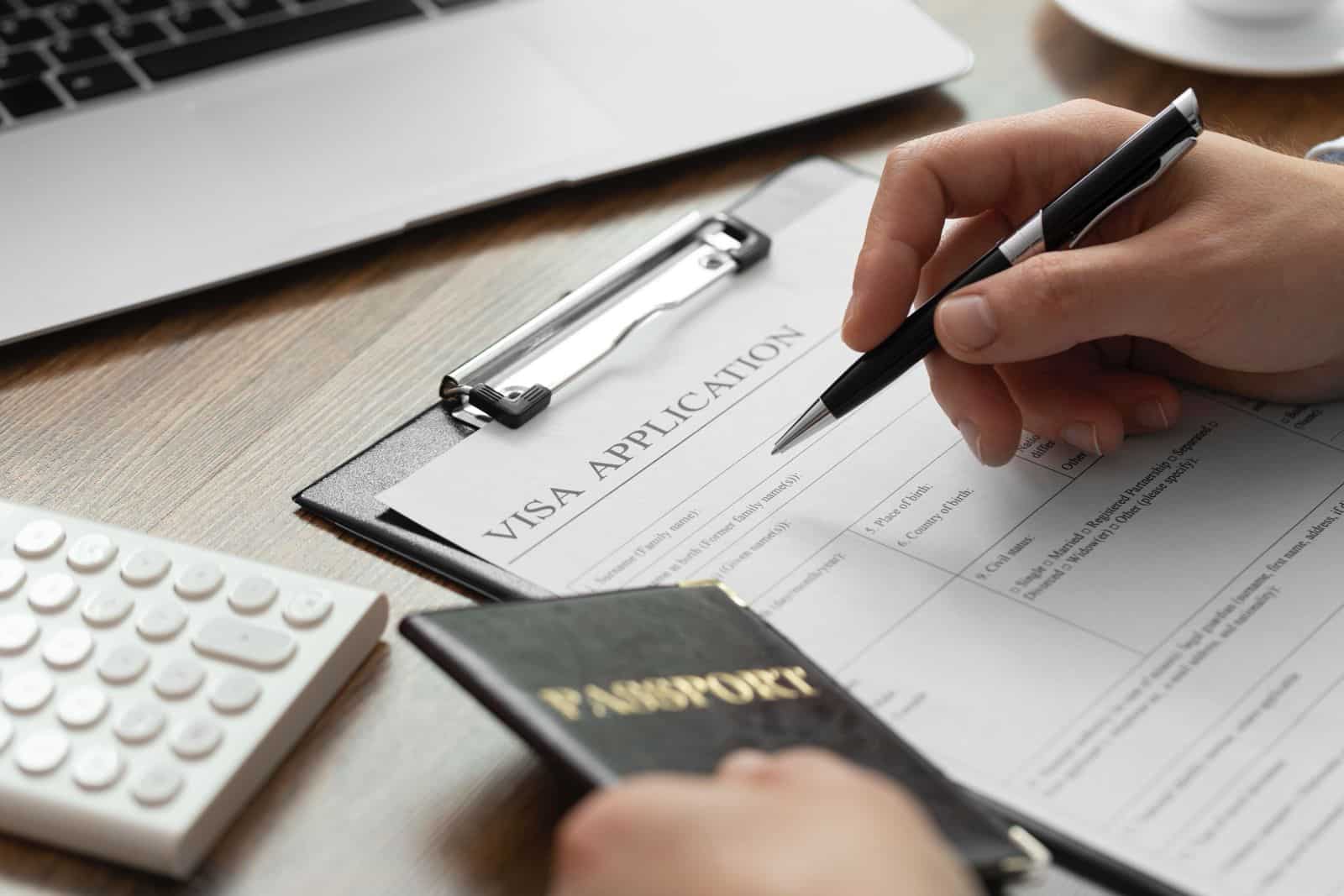 Hand holding a passport while filling out a visa application