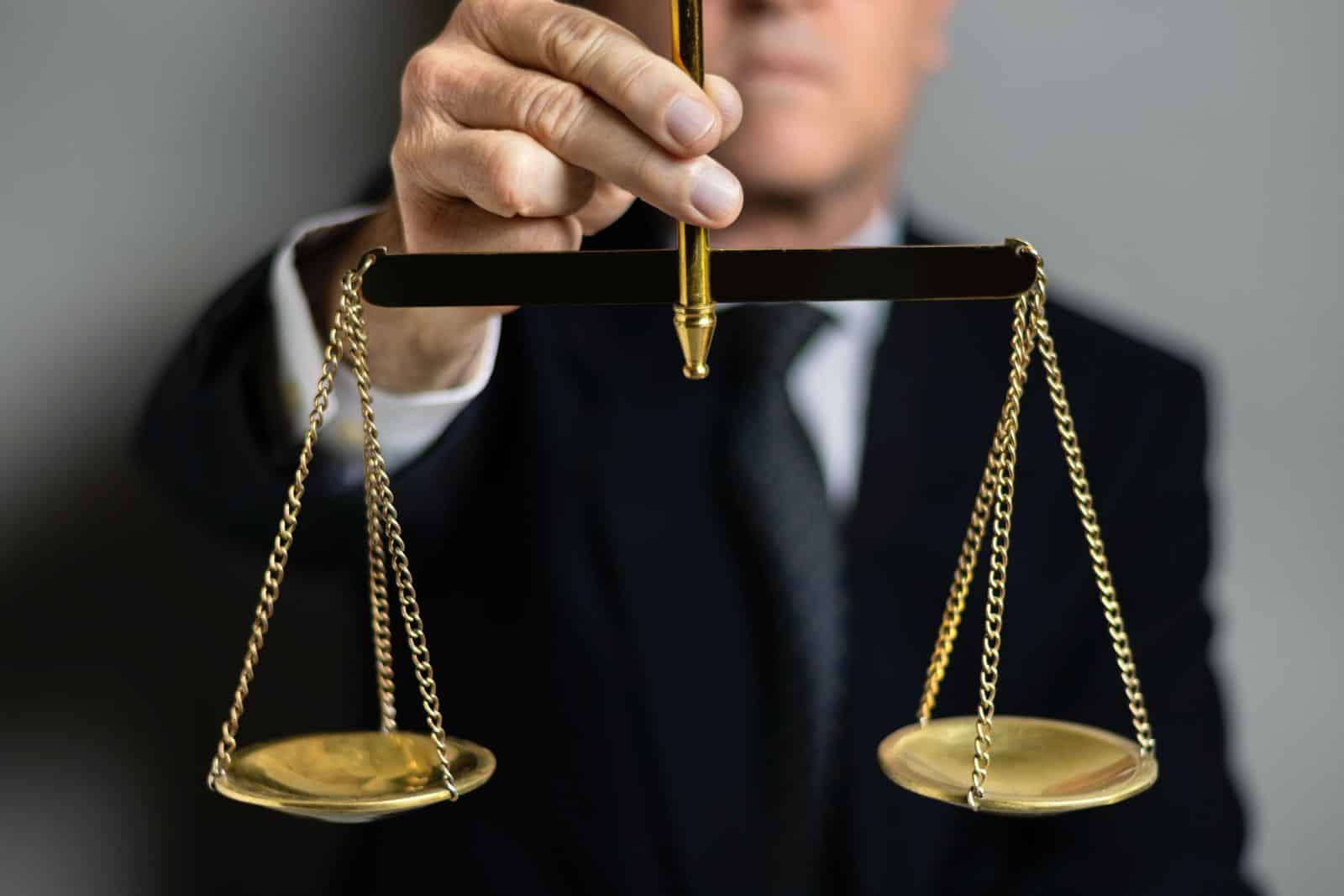 A person in a suit holding a gold balance scale.